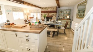 A kitchen with a large island, wooden cabinets, and a stone wall. - Kingfisher Cottage (Holmfirth)