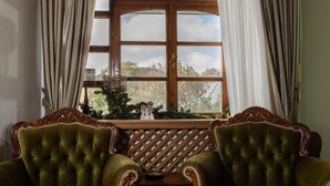 A room with two green upholstered chairs, a wooden table, and a window with a view of greenery. - Dandy Villas Nymfaio Snowfairy (Amyntaio)
