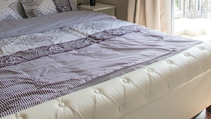 Een slaapkamer met een groot bed, een nachtkastje, een airconditioning en een raam met gordijnen.