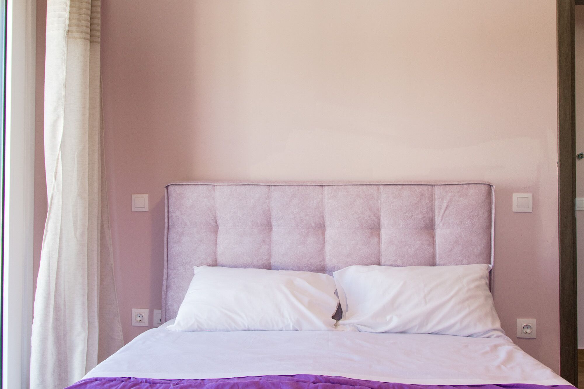 A bed with a headboard, two pillows, and a purple blanket.