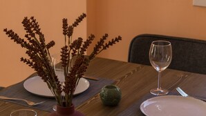Een eettafel gedekt met borden, bestek en een vaas met gedroogde bloemen.