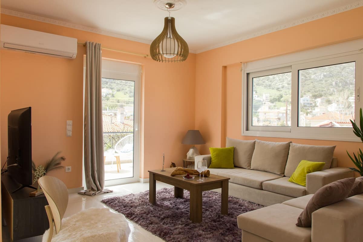 A living room with a sofa, a coffee table, and a TV. There is a window with a view of the outside.