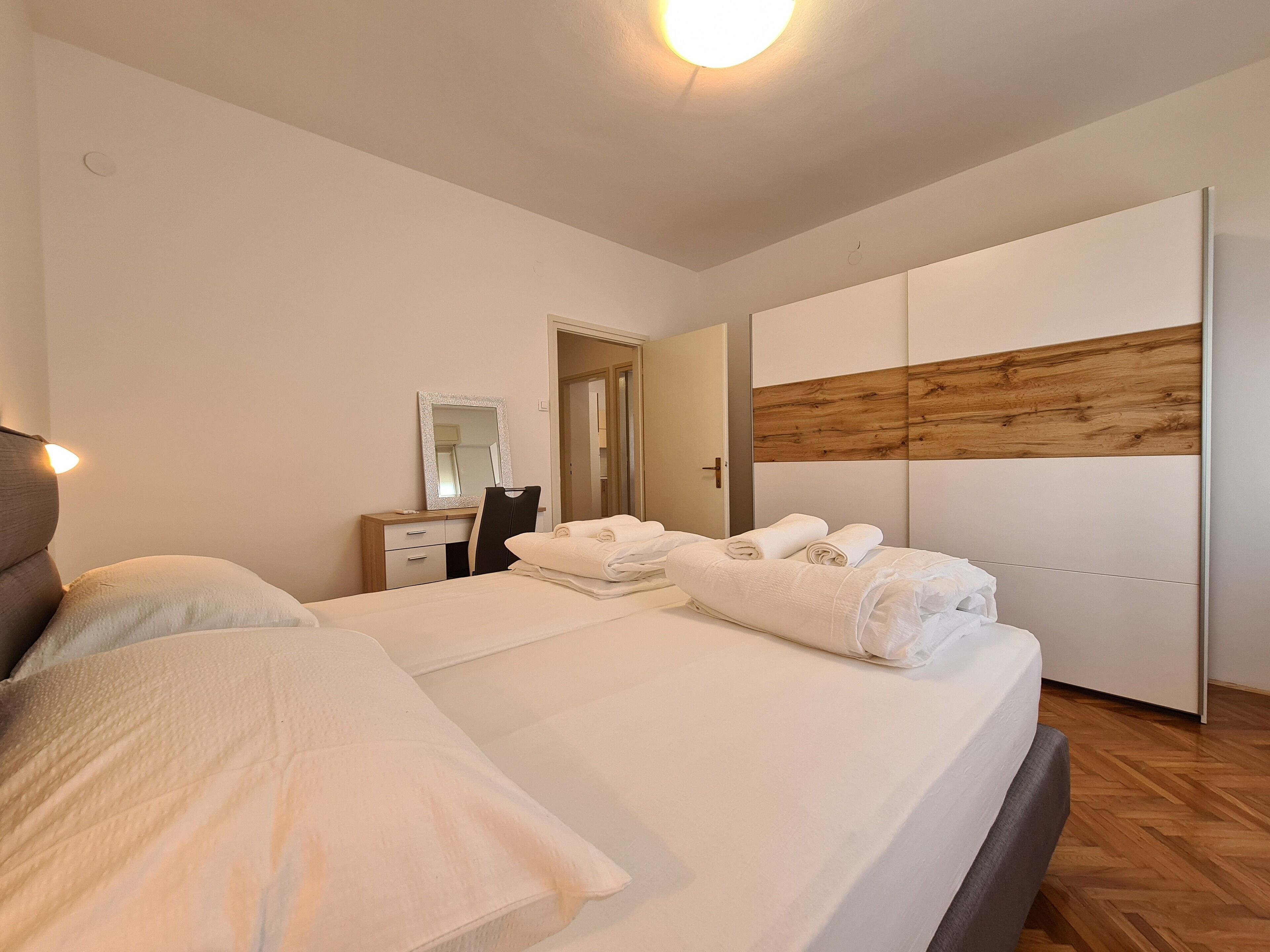 A modern bedroom with a large bed, a bedside table, a mirror, and a wardrobe.