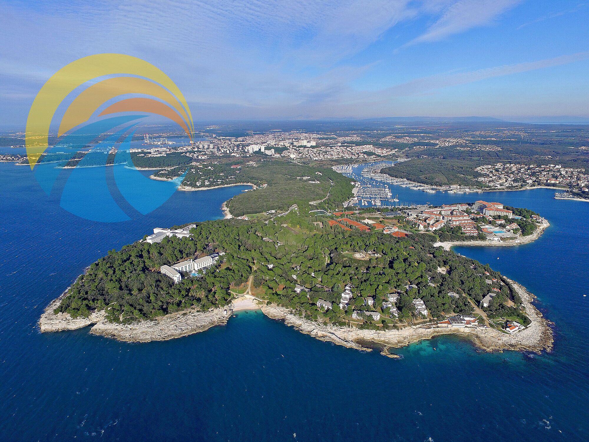 An aerial view of a coastal town with a marina, dense greenery, and residential areas.