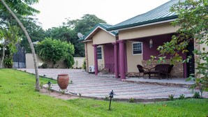Una casa con un patio empedrado, césped y una zona de comedor con sillas y una mesa.