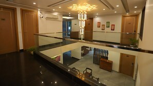 A modern hotel lobby with a glass railing, a central chandelier, and a seating area with a sofa and chairs. - Hotel Keshav Residency - Medicity Gurugram, near Medanta Hospital (Gurugram)