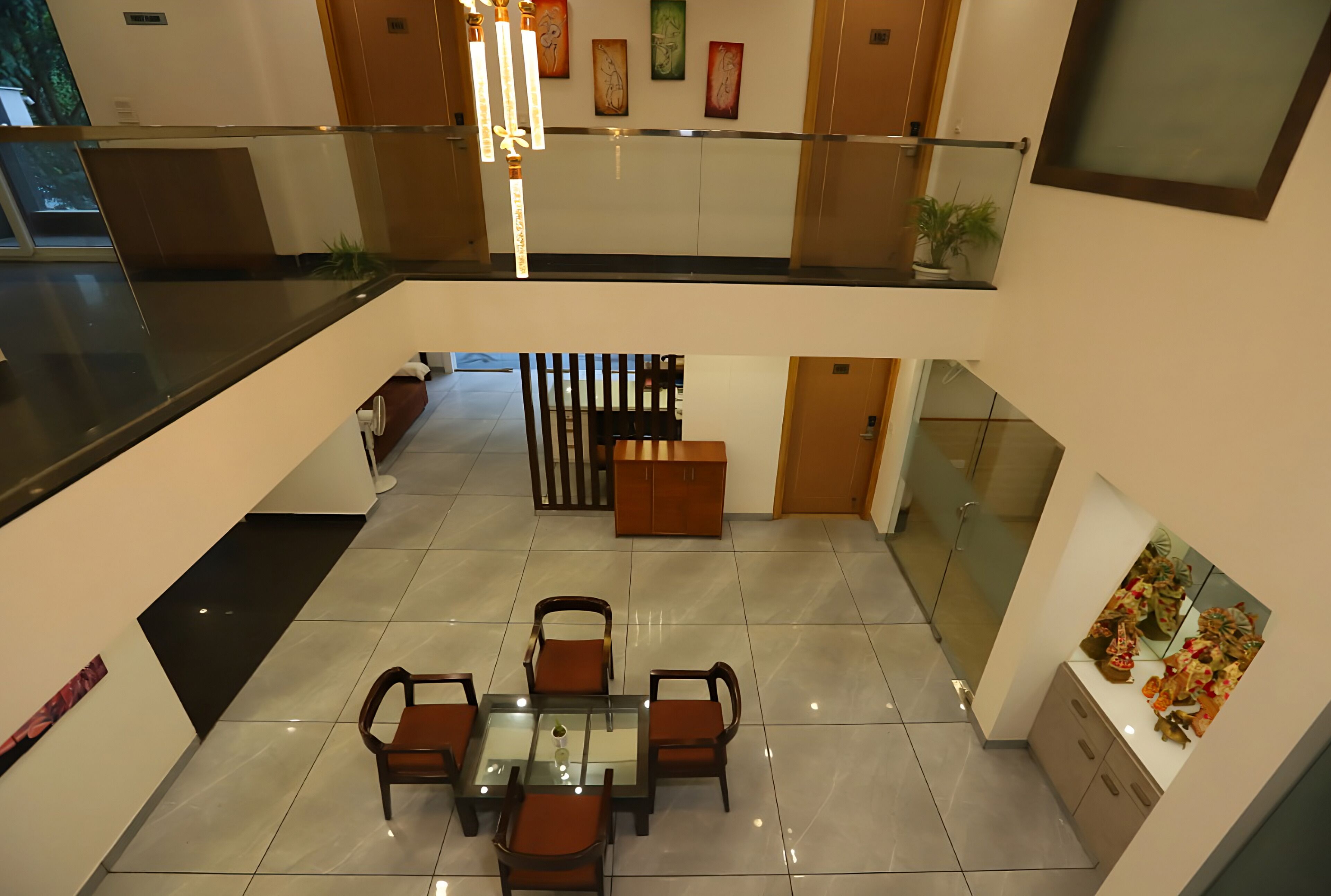 A spacious indoor area with a glass table and chairs, a wooden cabinet, and artwork on the walls.