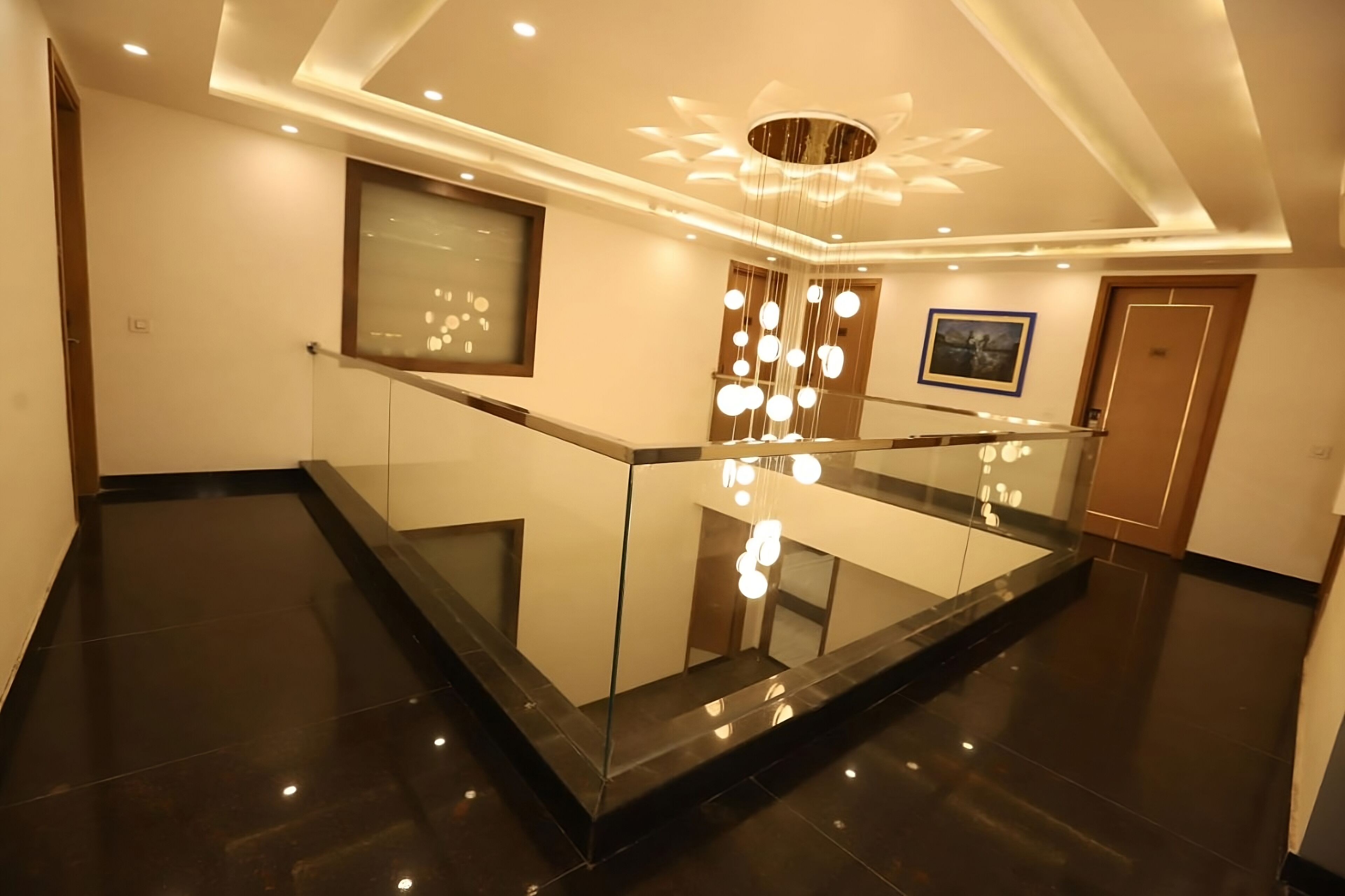 A modern hotel lobby with a glass railing, a chandelier, and a framed picture on the wall.