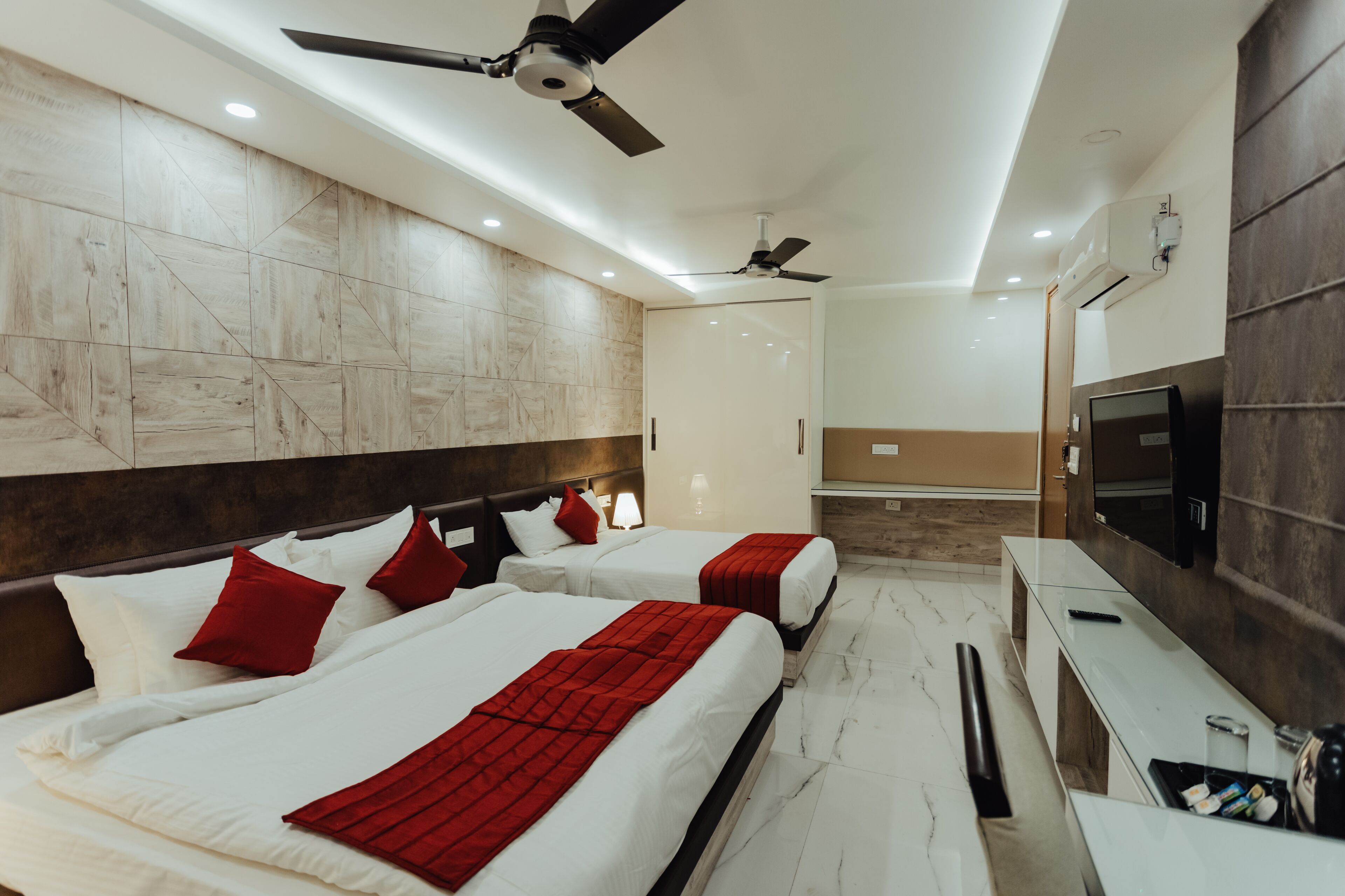 A hotel room with two beds, a TV, a desk, and a ceiling fan.