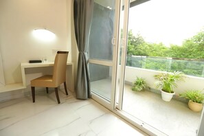 A balcony with potted plants, a desk with a chair, and a sliding glass door. - Hotel Keshav Residency - Medicity Gurugram, near Medanta Hospital (Gurugram)