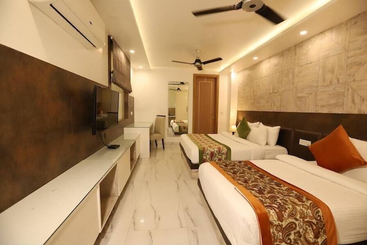 Una habitación de hotel con cama, mesita de noche, televisor, ventilador de techo y espejo.