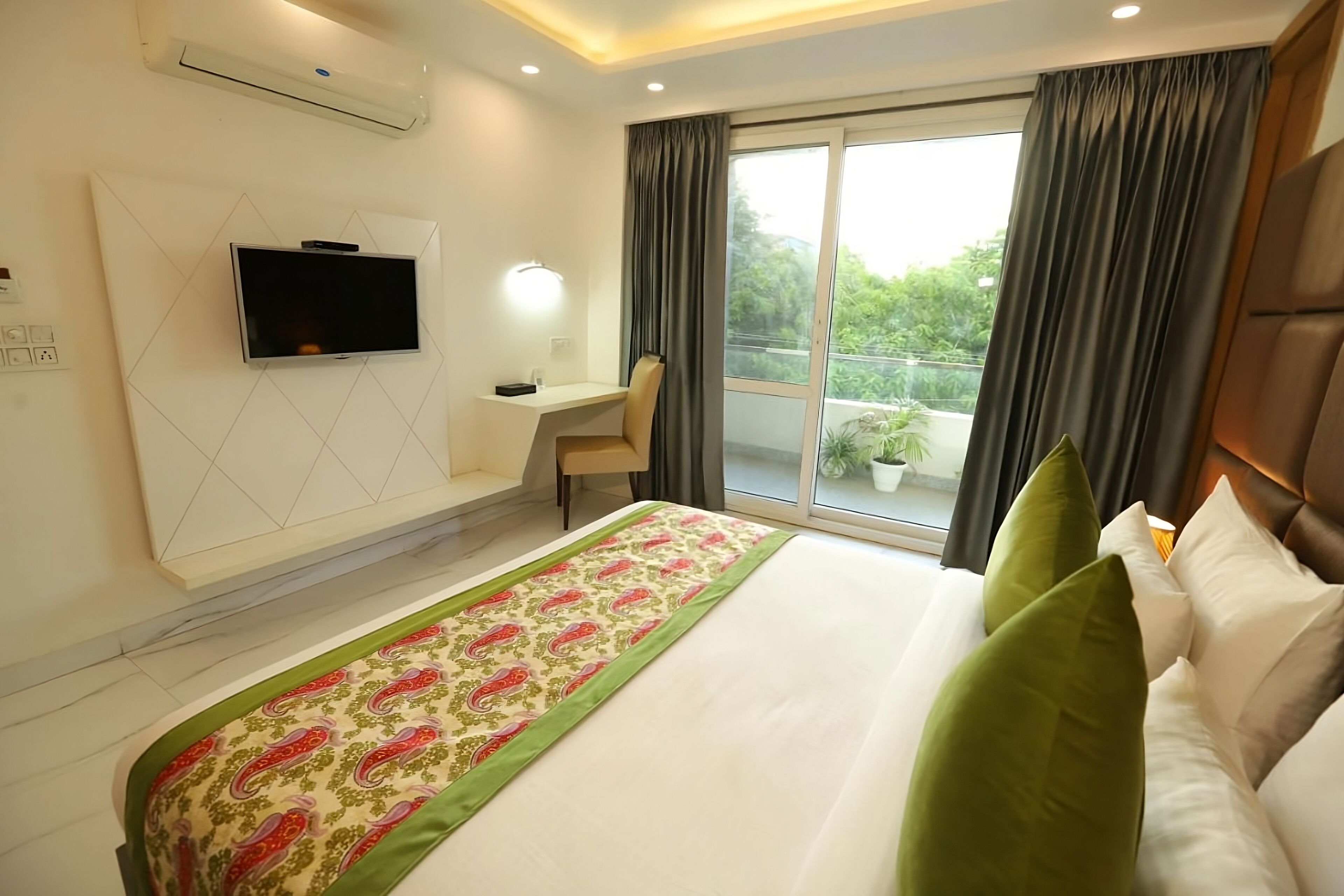 Quarto de hotel com cama, escrivaninha, televisão e janela com cortinas.