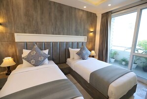 A hotel room with two beds, a wooden headboard, and a balcony with potted plants.