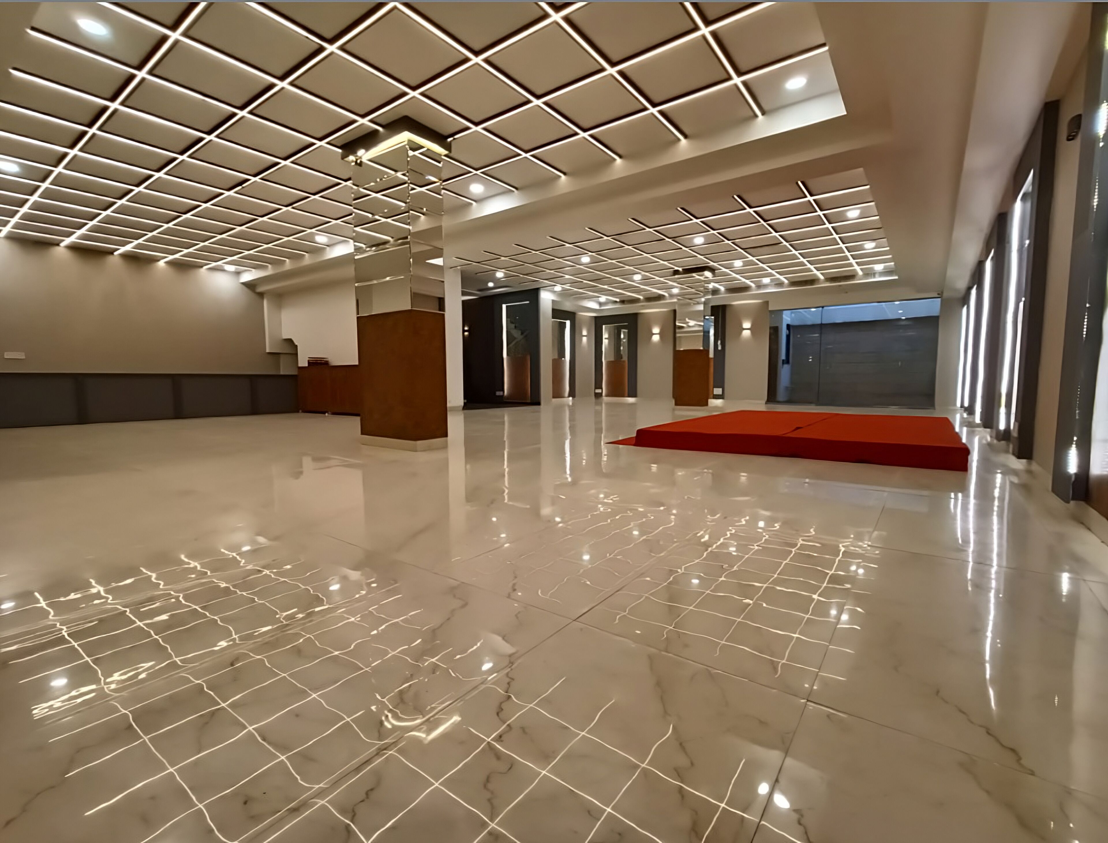 Un hall d’entrée spacieux doté d’un sol en marbre poli, d’une moquette rouge et d’un plafond au design moderne avec des luminaires encastrés.