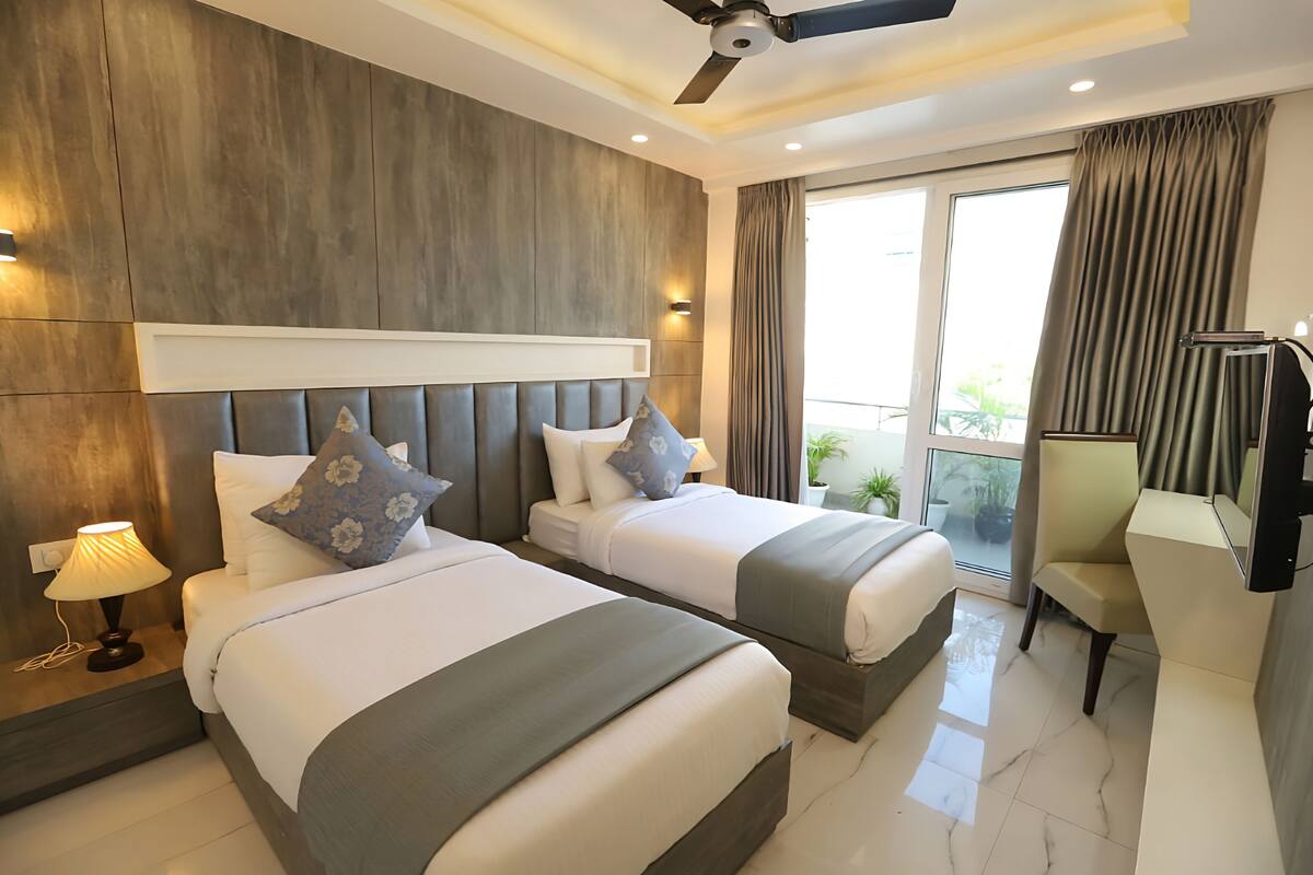 Habitación de hotel con dos camas, un ventilador de techo, un escritorio y vista al exterior.