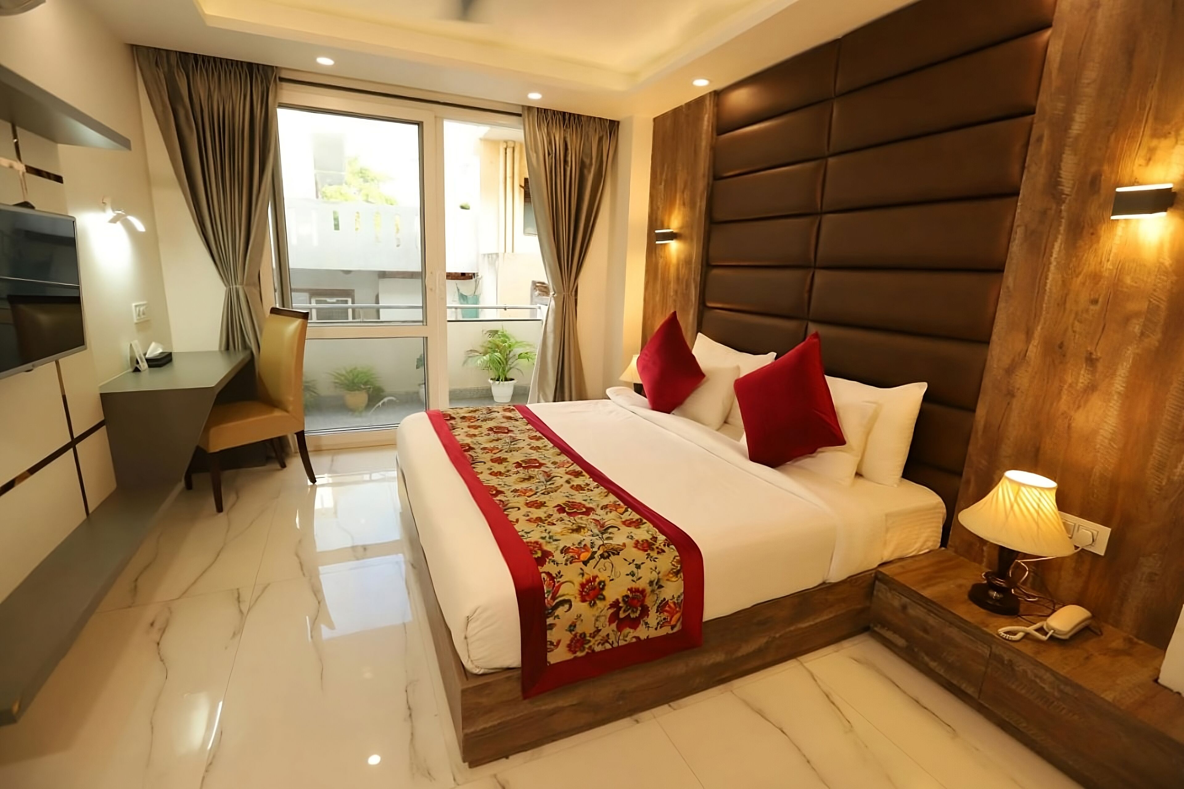 Habitación de hotel con una cama grande, un escritorio, una silla, un televisor y un balcón con una planta.