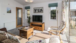 A spacious living room with a television, wooden furniture, a sofa, and a chair. - Meadow Lodge (Plymouth)