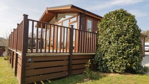 A wooden cabin with a deck, large windows, and a well-maintained garden. - Meadow Lodge (Plymouth)