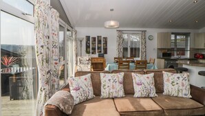 A living room with a sofa, dining table, and kitchen area. - Meadow Lodge (Plymouth)