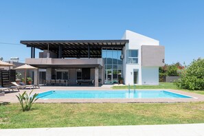 Een modern huis met twee verdiepingen, een zwembad, terrasmeubels buiten en een overdekt terras.