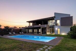 A modern two-story house with a swimming pool, outdoor seating, and a covered patio.