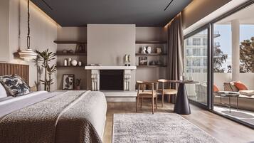 A modern bedroom with a large bed, a fireplace, a dining area, and a balcony with a view of the city.