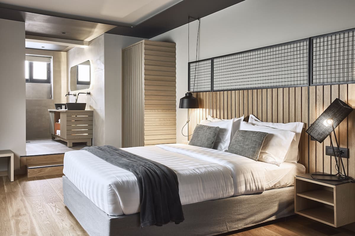 A modern bedroom with a large bed, bedside tables, a nightstand, a mirror, and a window.