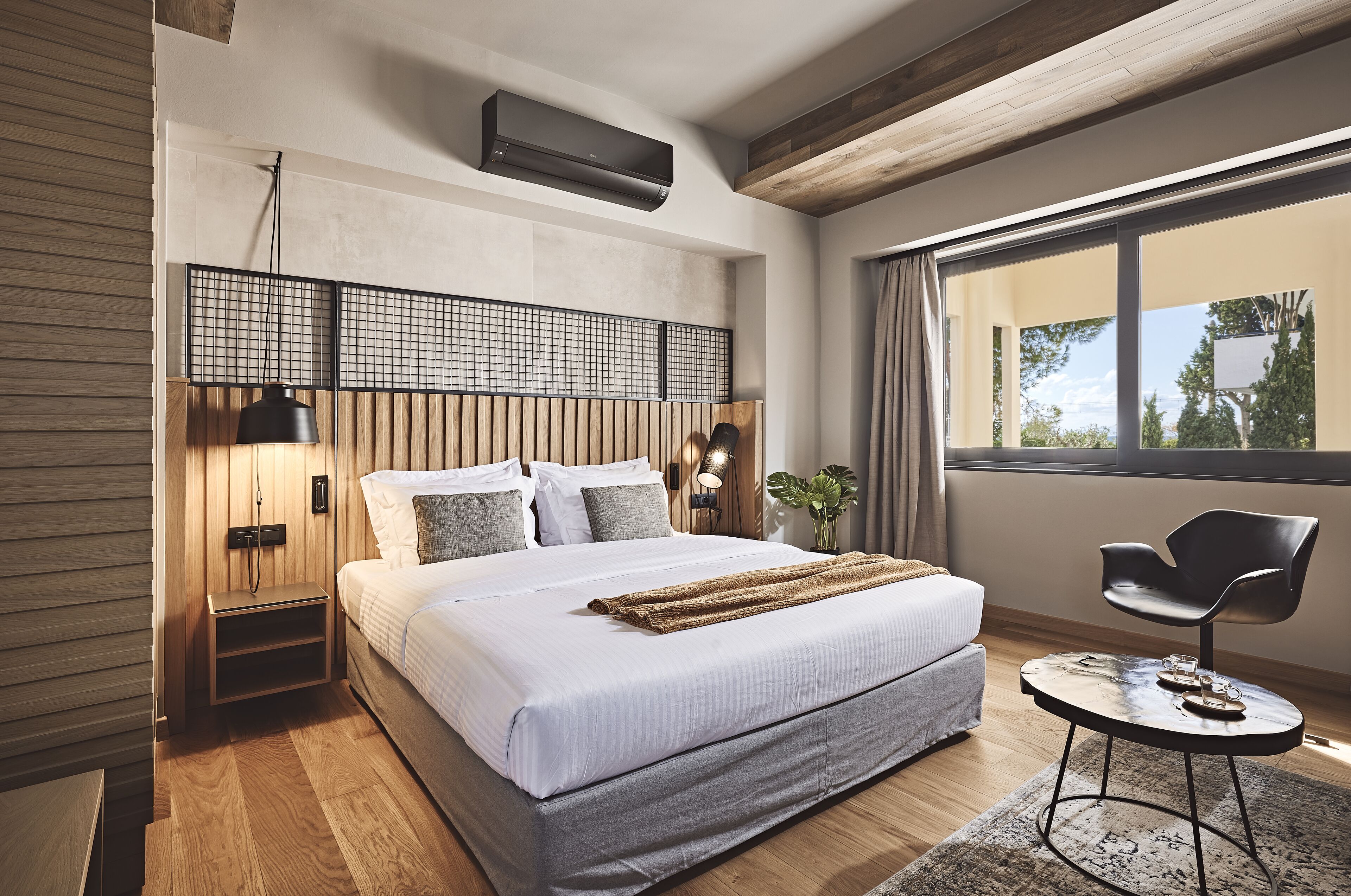A modern bedroom with a large bed, a bedside table, a chair, and a window with a view.