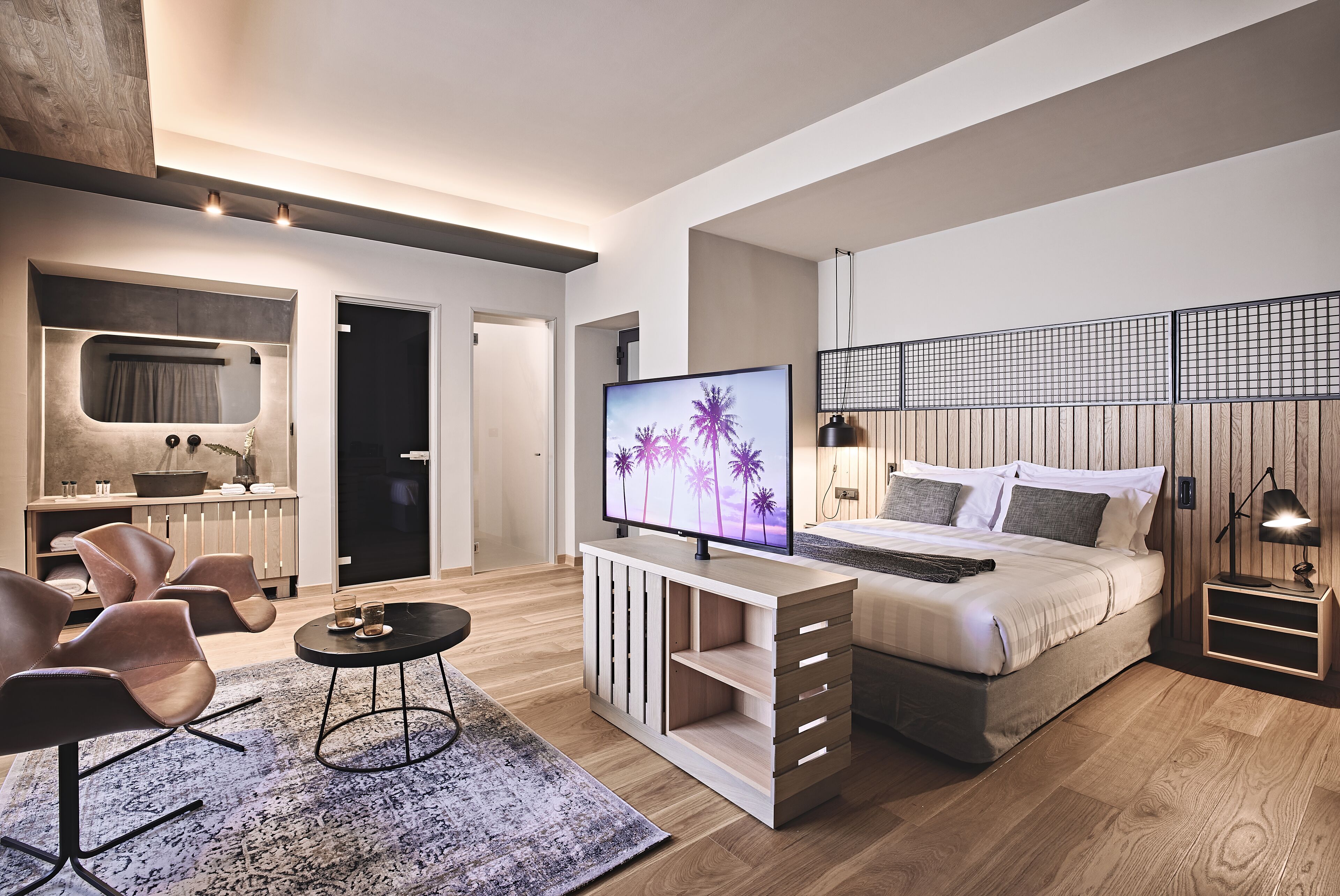 A modern bedroom with a bed, a TV, a desk, and a seating area.