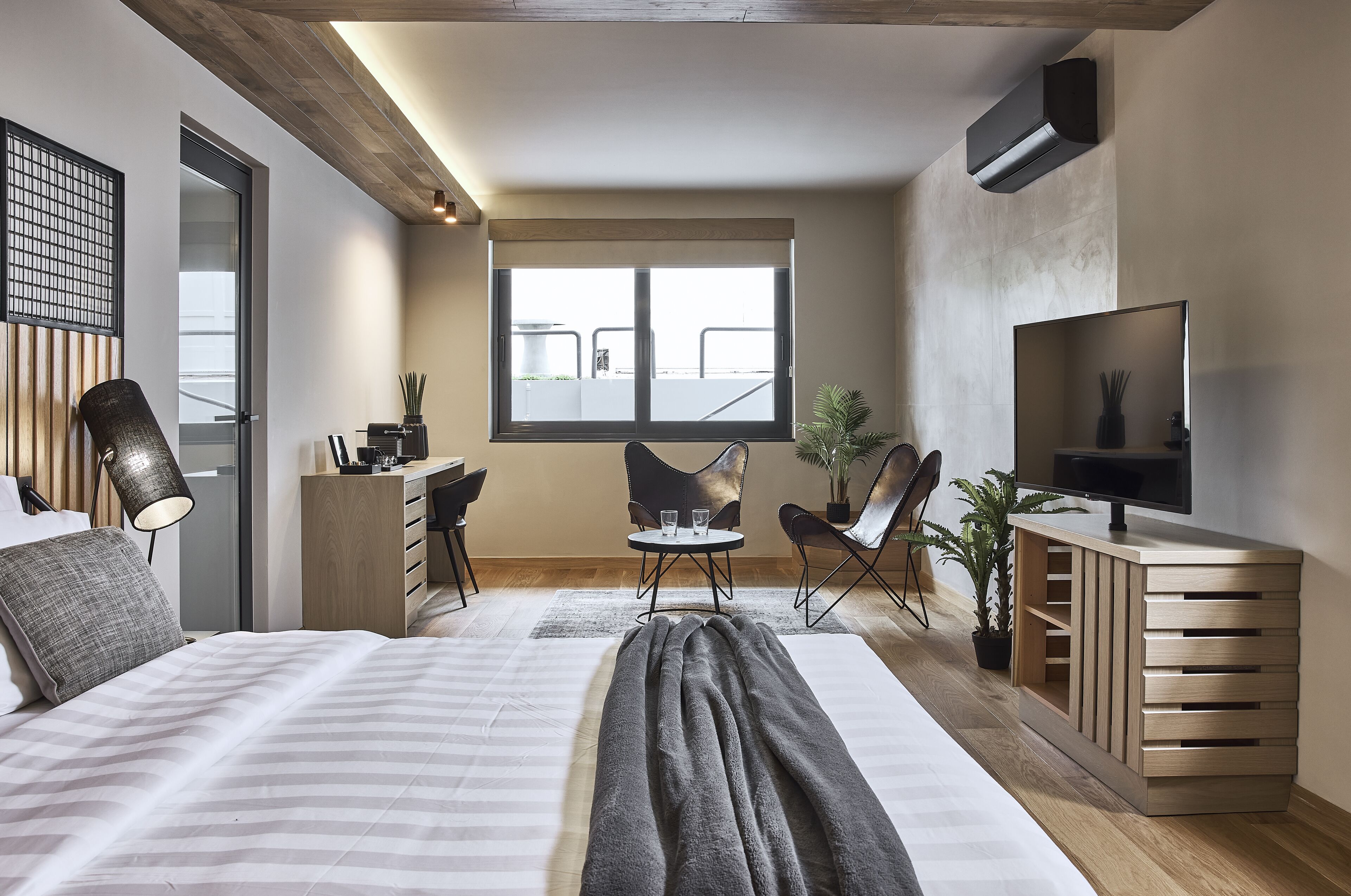 A modern hotel room with a large bed, a desk, two chairs, a TV, and a window with a view.