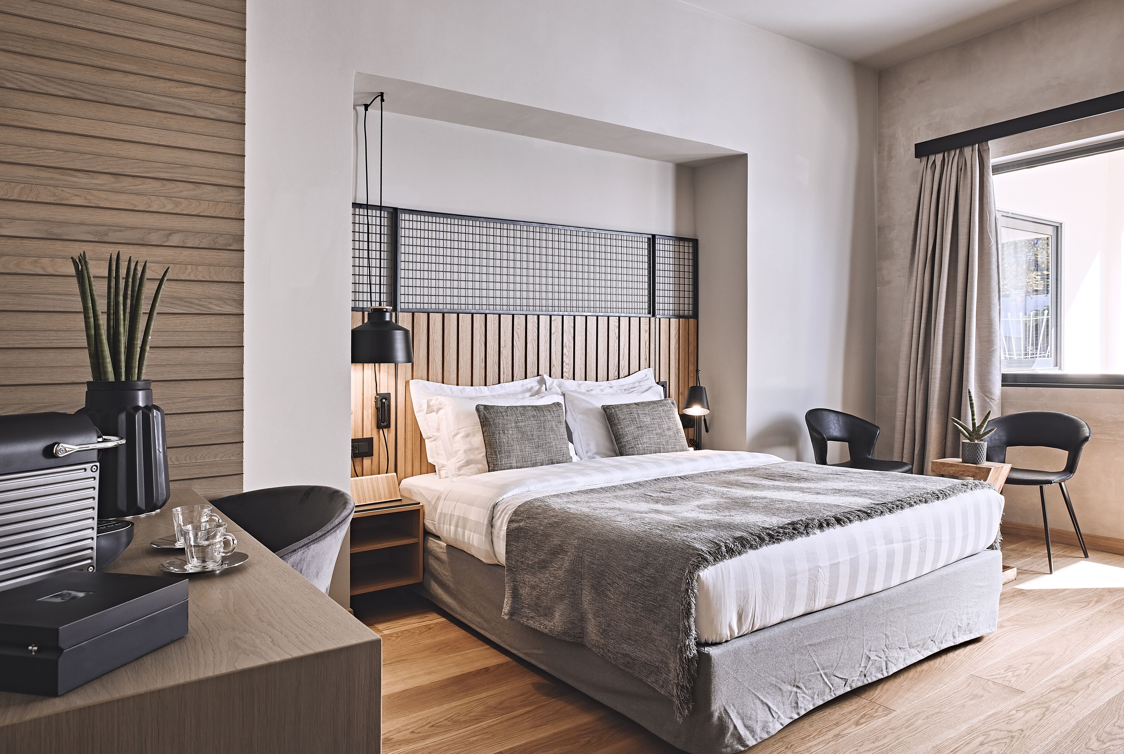 A modern bedroom with a large bed, bedside tables, a desk, and a potted plant.