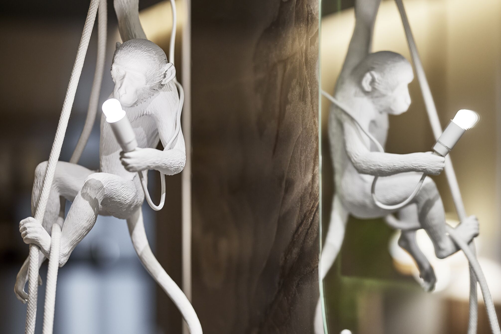 Escultura de una figura sentada sosteniendo una fuente de luz, con un fondo desenfocado.