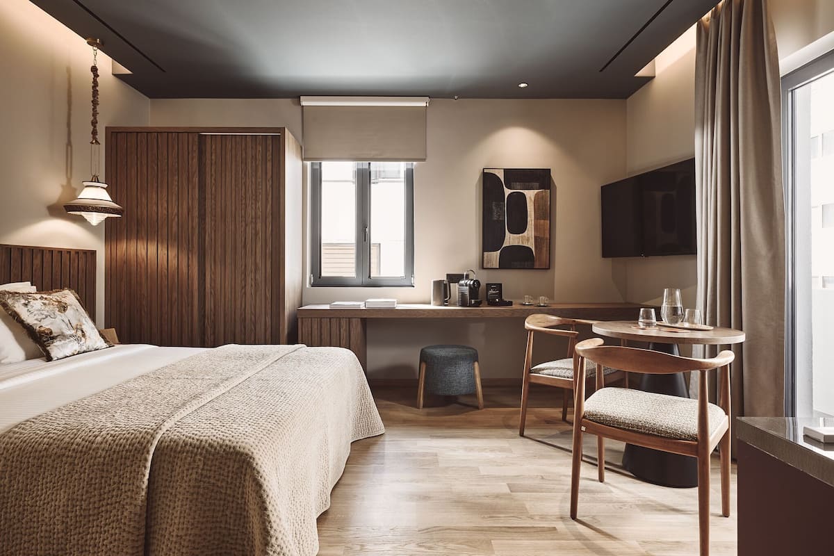 A modern hotel room with a bed, desk, chair, and a large window.