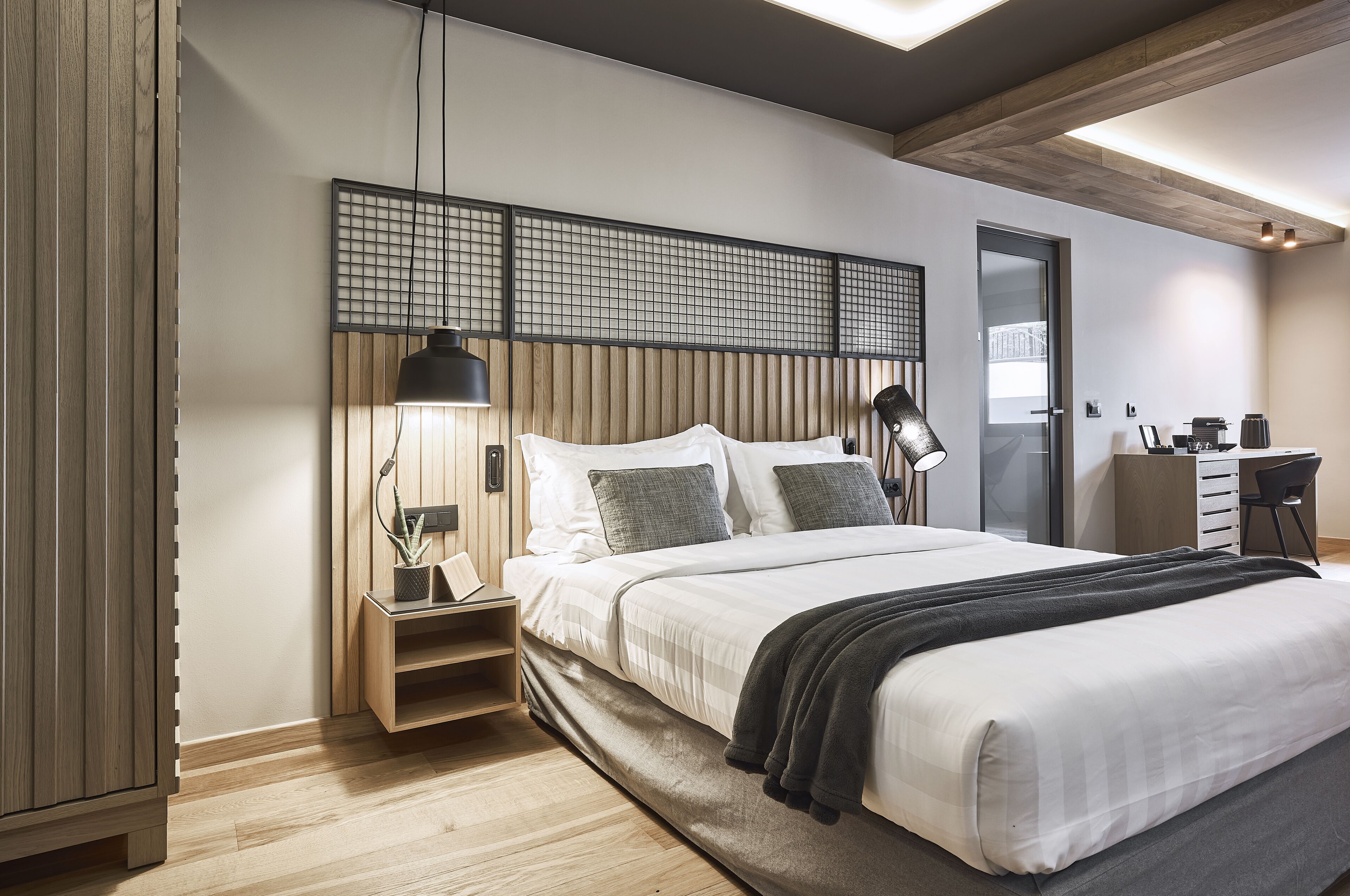 A modern bedroom with a large bed, bedside lamps, a wooden headboard, and a desk area with a chair.