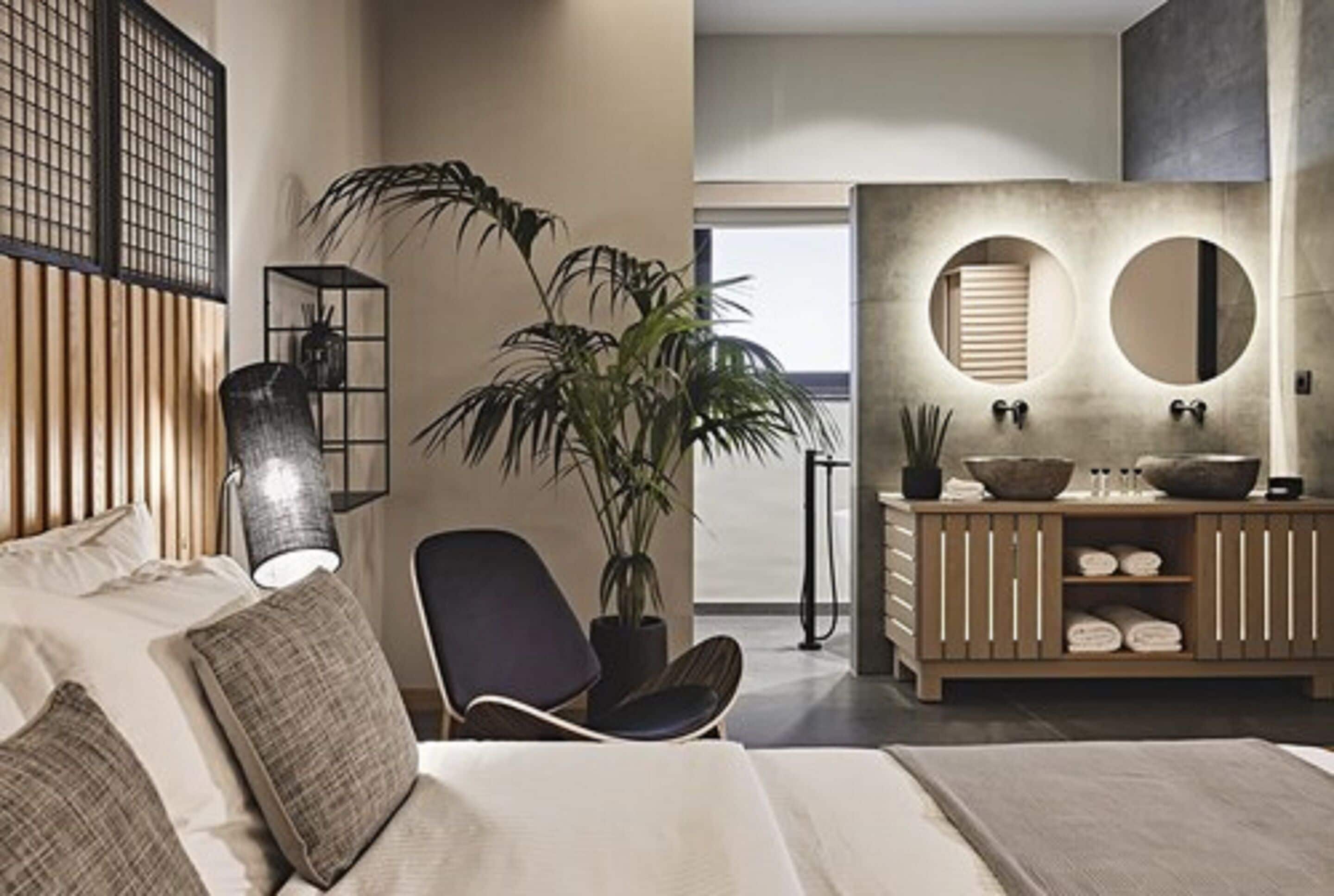 A modern bedroom with a bed, bedside table, lamp, chair, and a large potted plant.