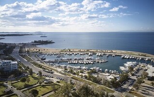 A marina with boats docked, a road leading to the marina, and a beach in the background.