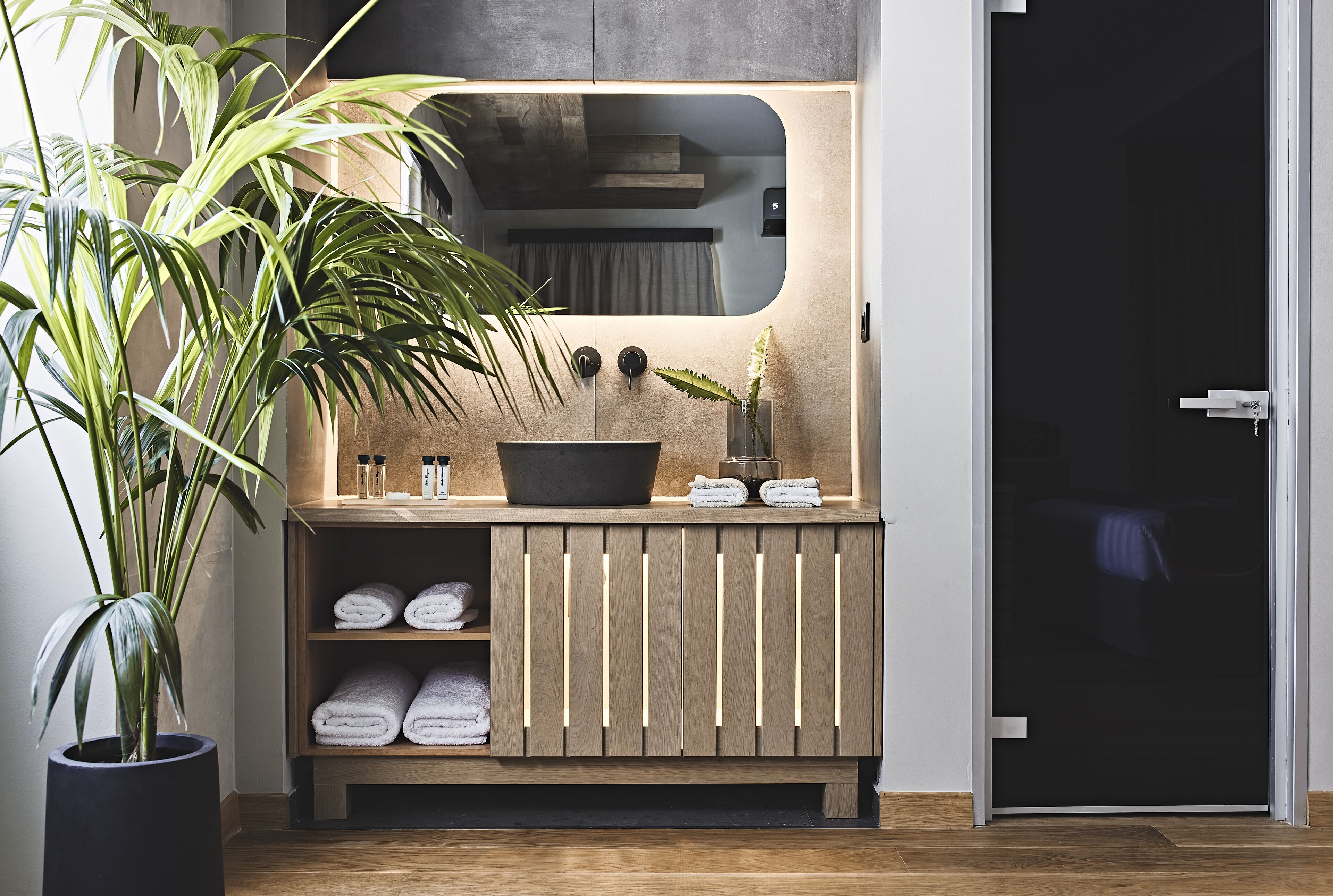 A modern bathroom with a wooden vanity, a large mirror, and a potted plant.