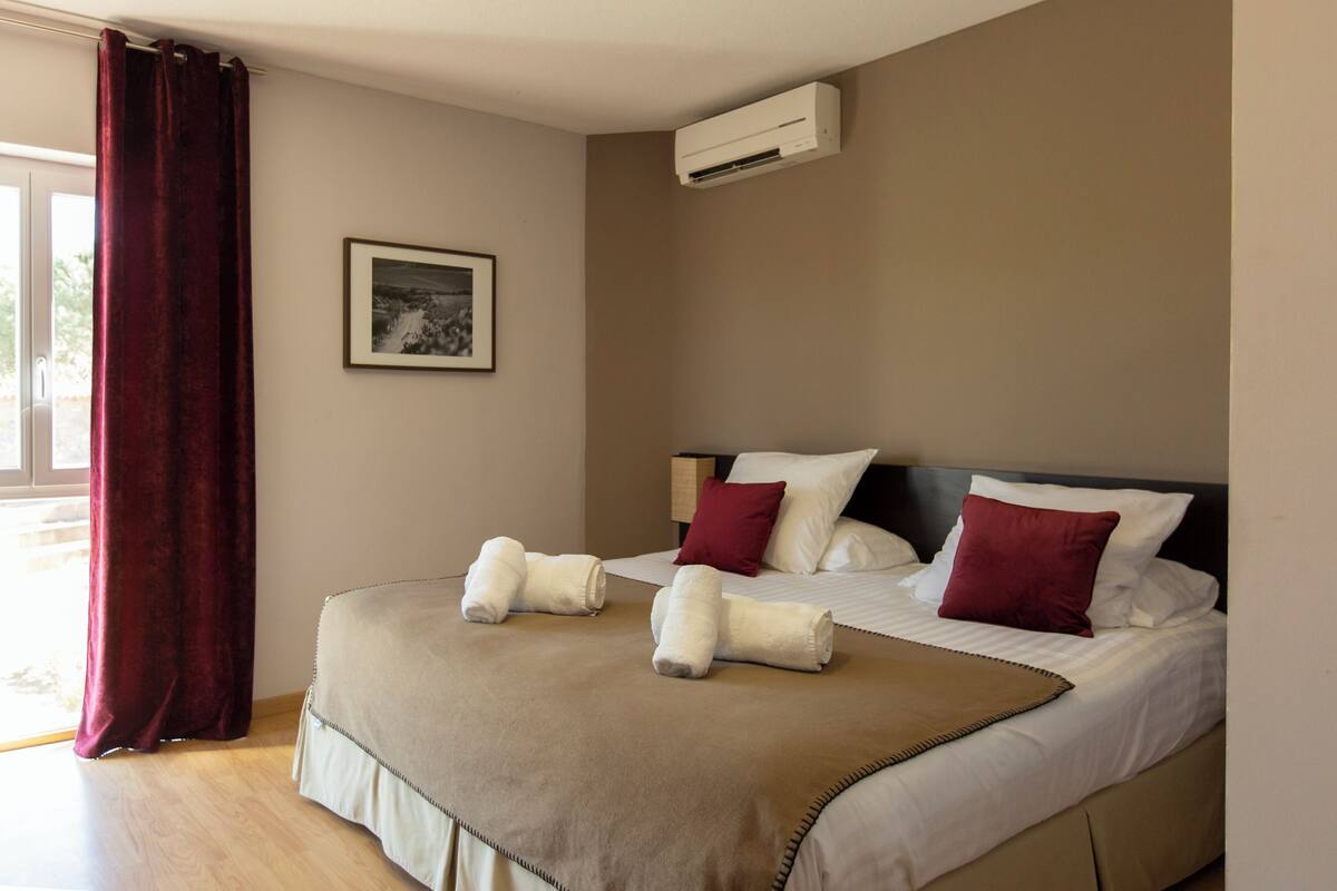 Une chambre d’hôtel avec un lit, une fenêtre avec des rideaux, un appareil de climatisation et un tableau encadré au mur.