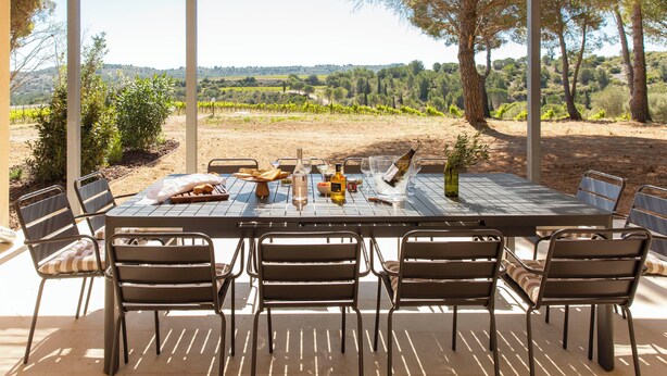 An outdoor dining area with a table set for six, surrounded by chairs, overlooking a vineyard and hilly landscape. - Les Villas du Château de Lastours (Portel-des-Corbières)
