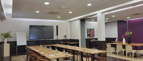 A conference room with a long table, chairs, a projector screen, and a whiteboard.