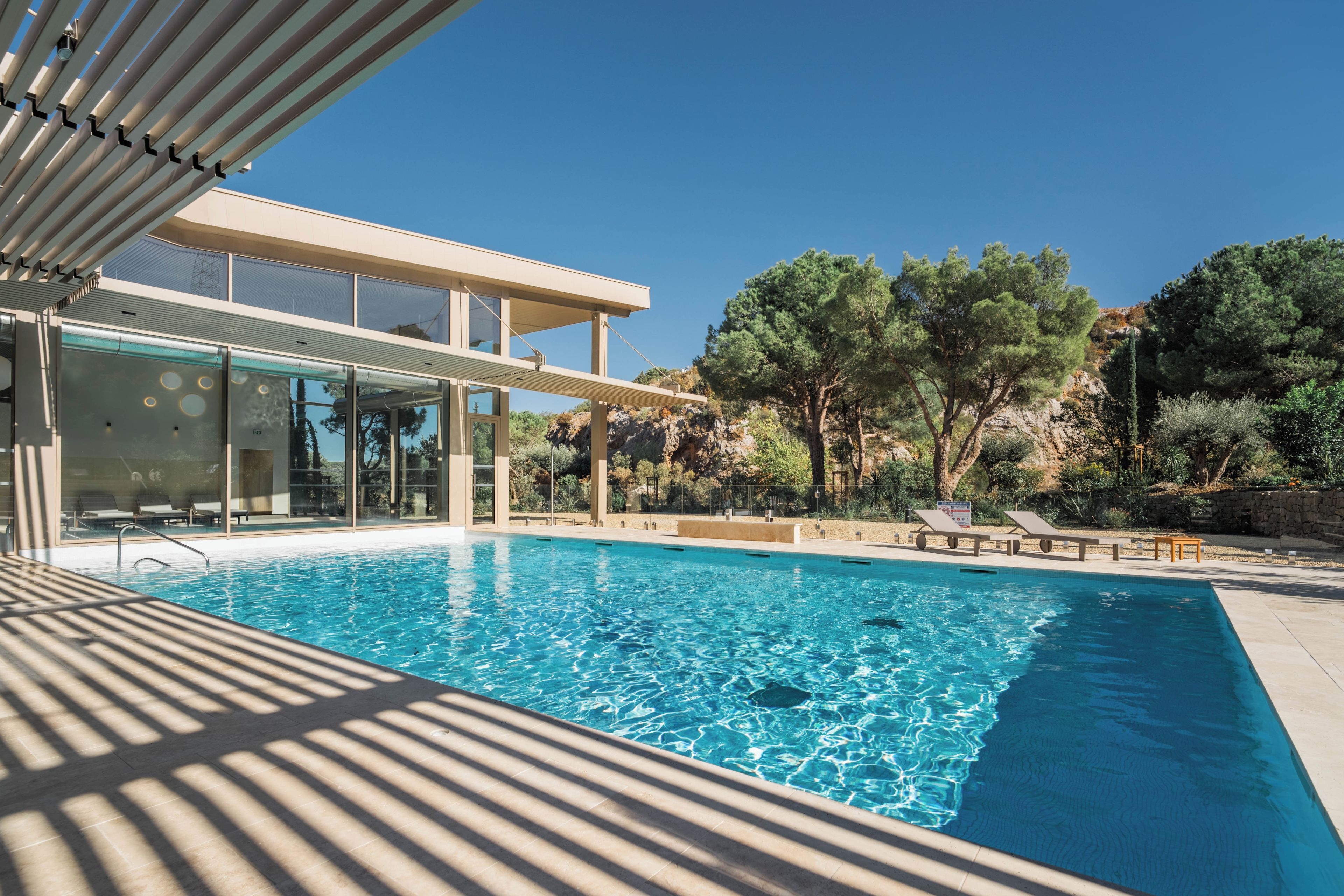 A modern pool area with clear blue water, a covered seating area, and a view of surrounding trees and landscape.