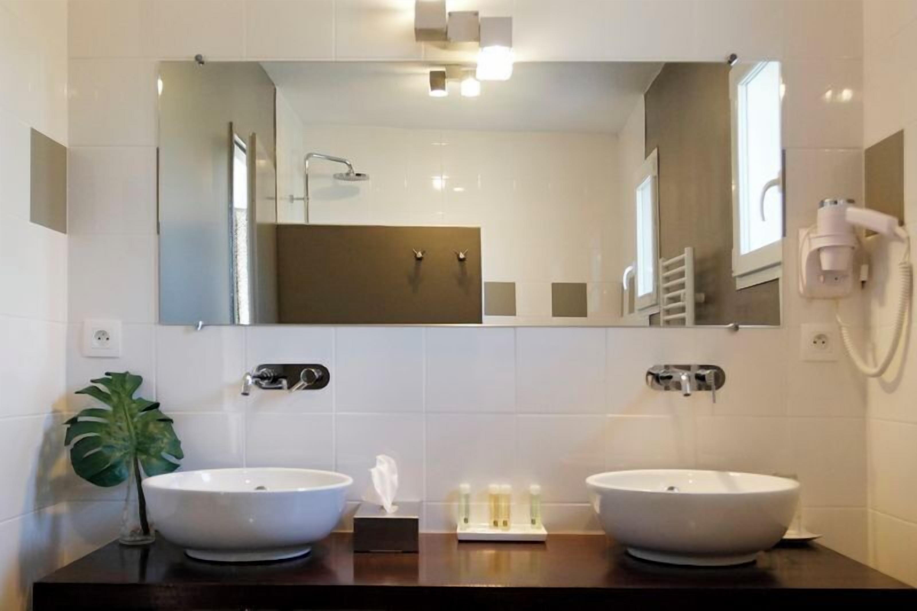 Een moderne badkamer met twee wasbakken, een grote spiegel en een haardroger bevestigd aan de muur.