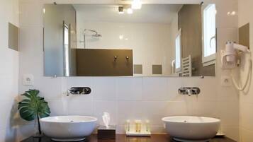 Een moderne badkamer met twee wasbakken, een grote spiegel en een haardroger bevestigd aan de muur.