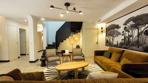 A modern living room with a staircase, a large painting, and a coffee table. - Les Villas du Château de Lastours (Portel-des-Corbières)