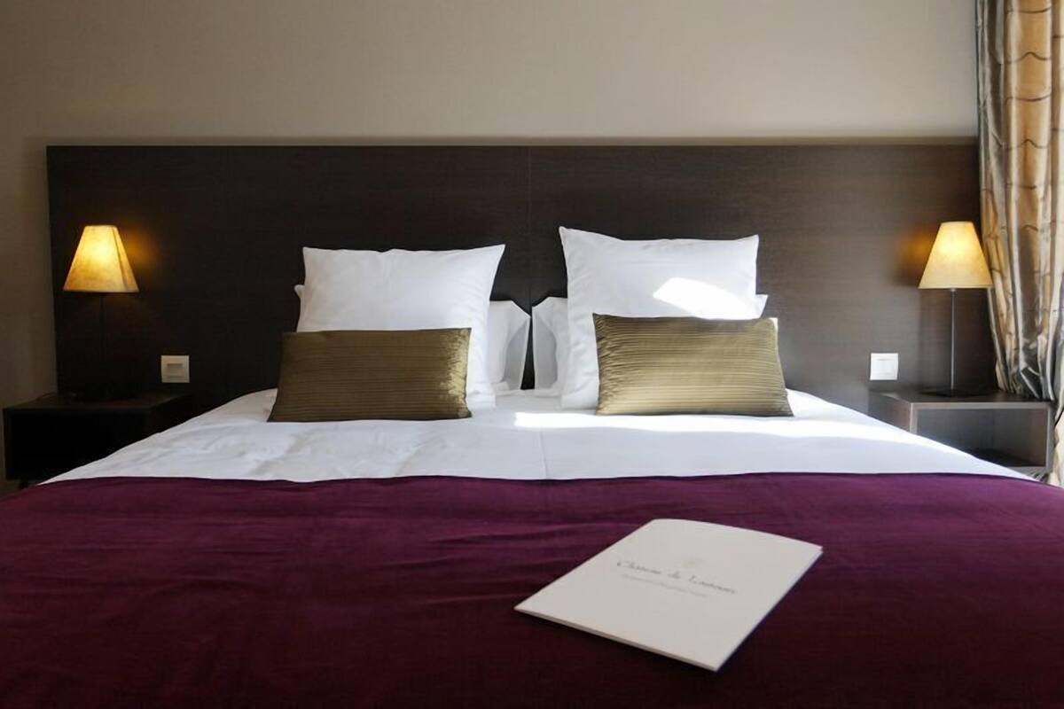 Un lit bien fait, agrémenté d’oreillers blancs et dorés, d’une couvre-lit violette et d’un livre intitulé « Chambre de Luxe » posé sur le lit.