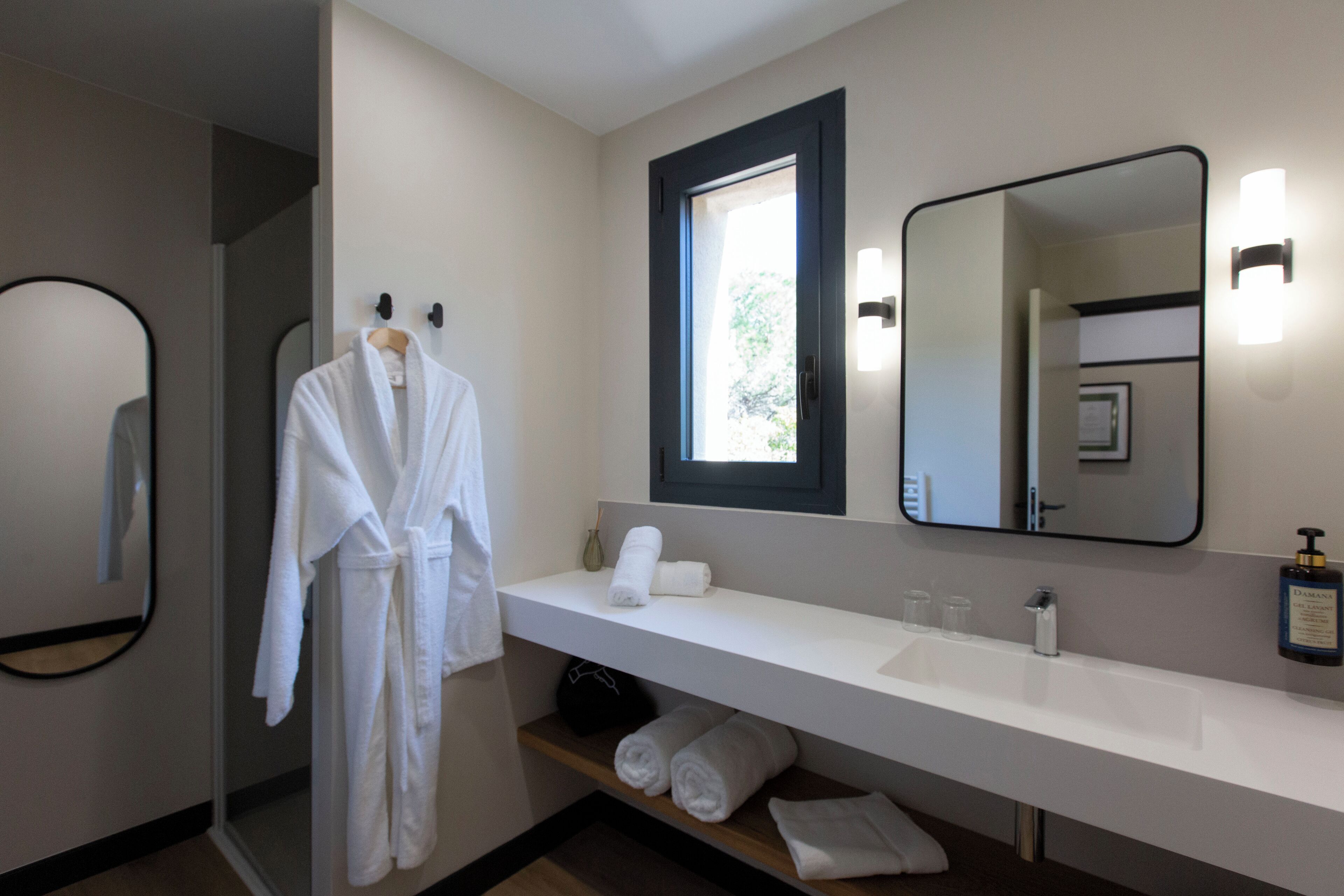 Un baño moderno con un tocador blanco, un espejo grande y una bata colgada en un perchero.