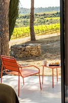 Un patio con una mesa, una silla, un muro de piedra y vistas a un viñedo.