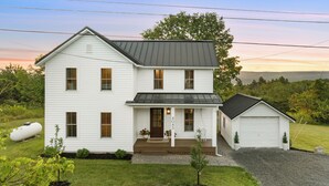 A two-story white house with a front porch, a garage, and a small detached shed.