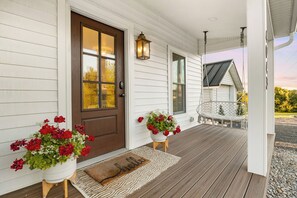 A wooden porch with a brown door, two potted plants, a bench, and a swing.