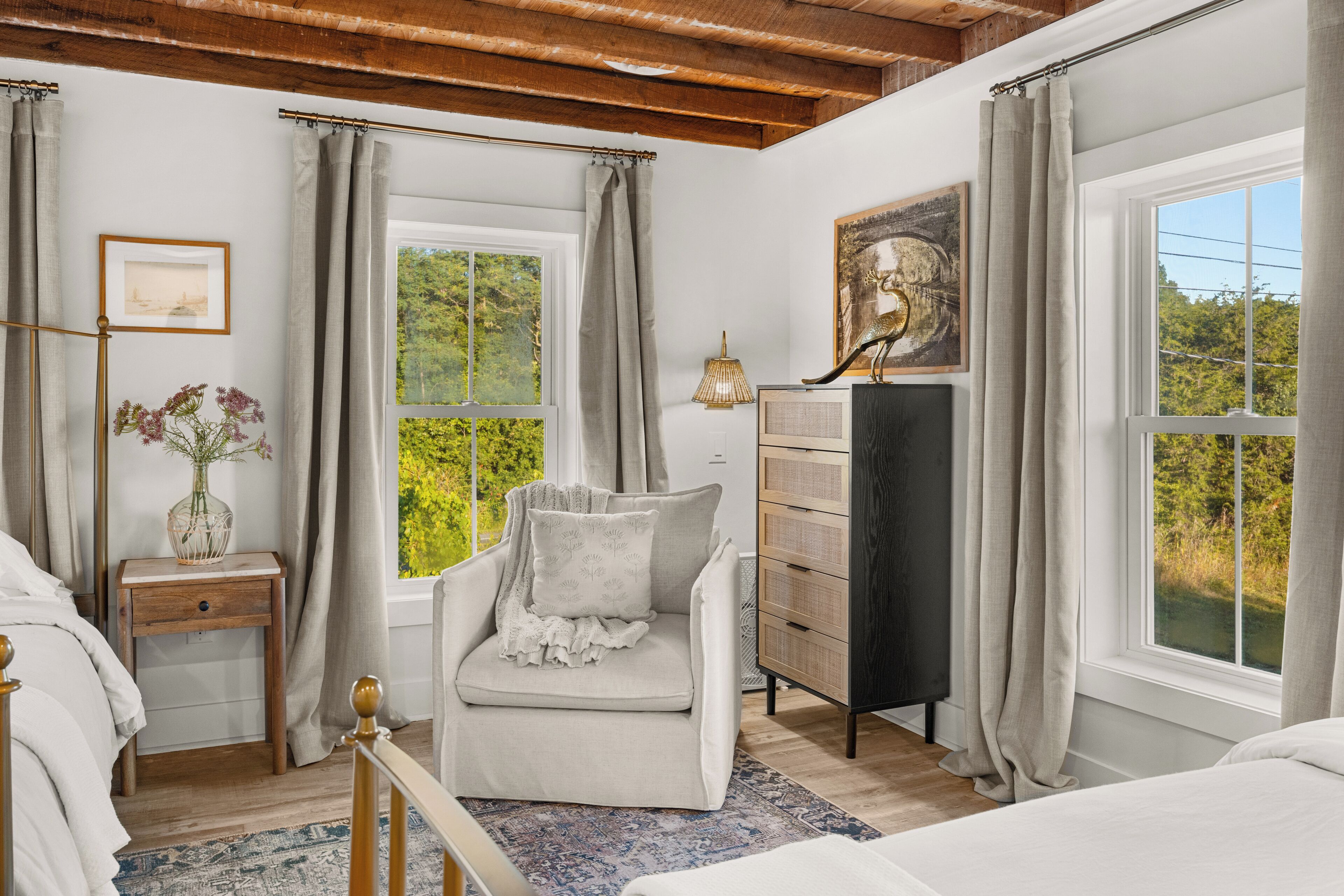 Une chambre à coucher comprenant un lit, une chaise, une commode, une lampe et une fenêtre donnant sur un paysage verdoyant.